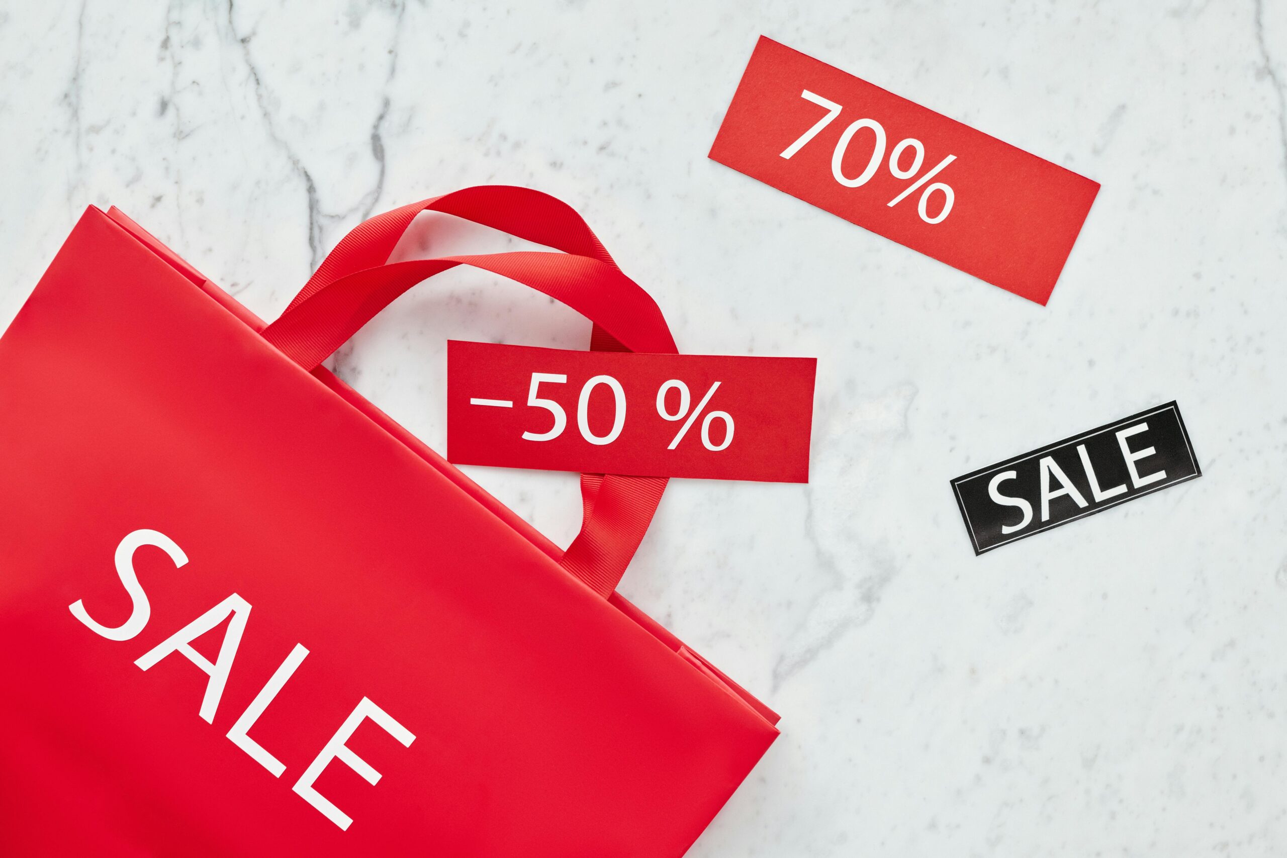 Red sale bag with 50% and 70% discount tags on marble background, perfect for retail promotions.