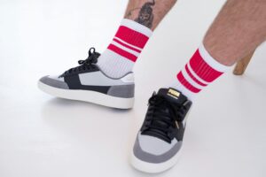Close-up of sneakers paired with striped socks and tattoo, offering a trendy footwear style.