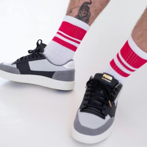 Close-up of sneakers paired with striped socks and tattoo, offering a trendy footwear style.